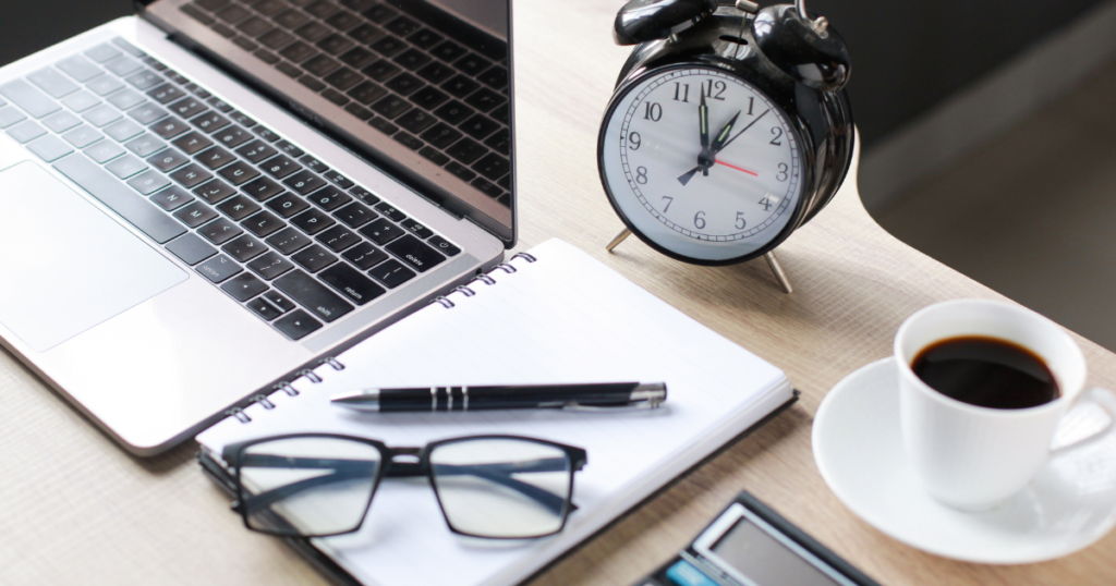 Laptop, notebook, clock, and coffee on an office desk